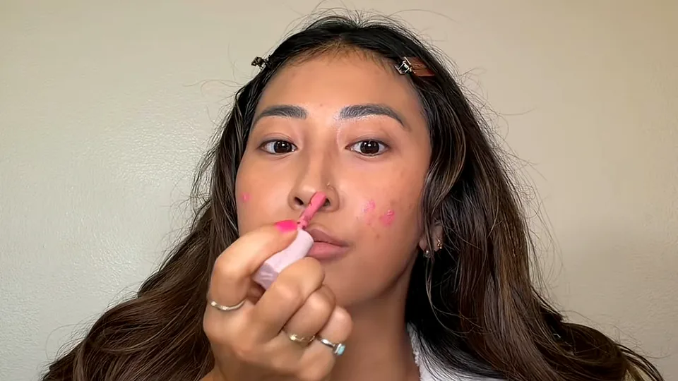 Creator dabbing pink liquid blush onto her cheeks with a doe-foot applicator