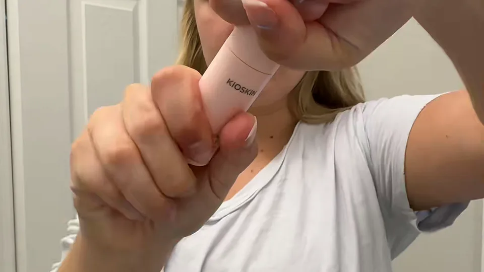 Creator in a grey T-shirt twisting open a pink Kioskin skincare tube with both hands