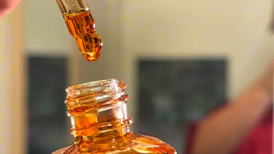Glass dropper releasing a drip of amber serum into the open neck of the bottle