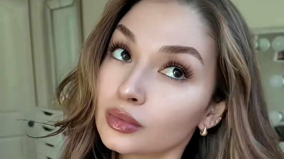 Creator with full glam makeup, glossy lips and lifted lashes glancing sideways at the camera