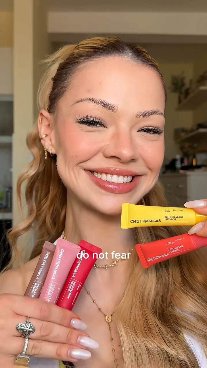 Creator smiling at camera and fanning out lip gloss tubes