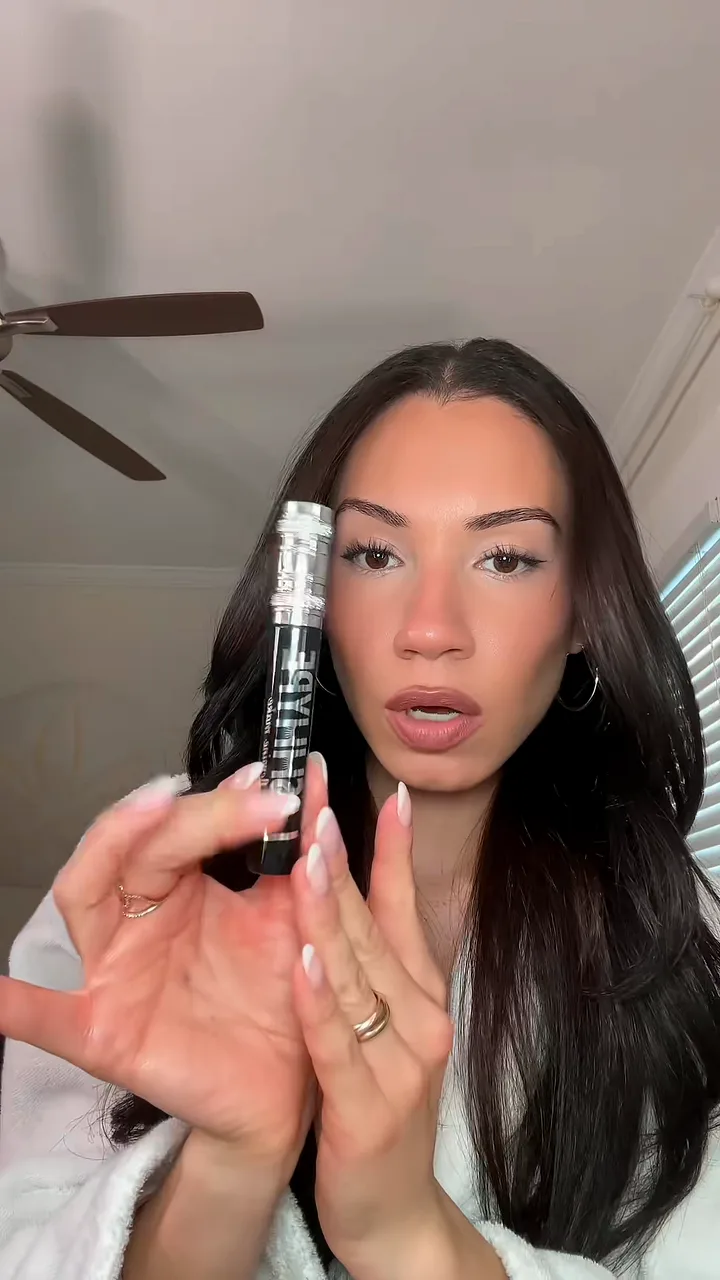 Creator in a white robe holding up a mascara wand