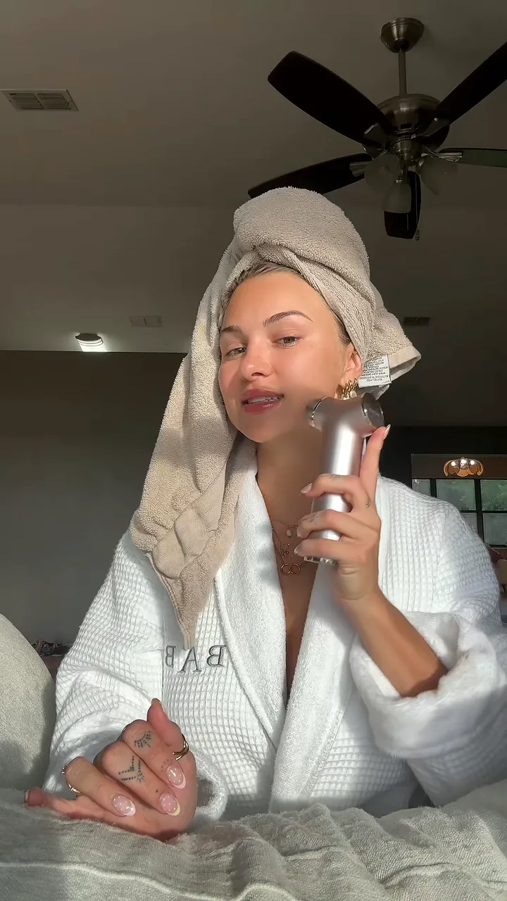 Creator in a towel turban holding a skincare device to her cheek