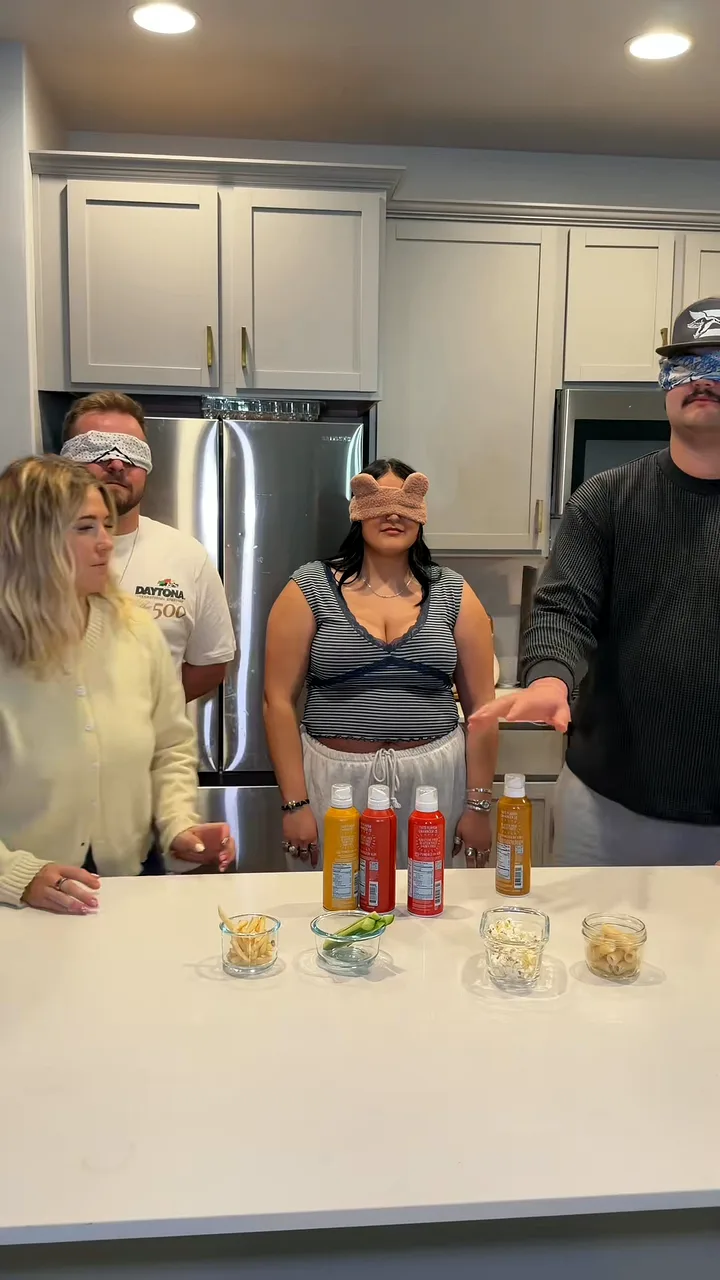 Group of friends, several blindfolded, holding flavour sprays in a kitchen
