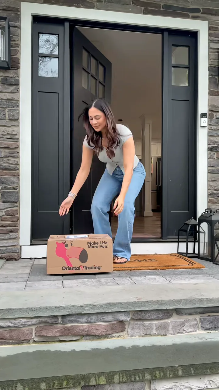 Woman stepping out of a black front door to pick up an Oriental Trading box from the doorstep