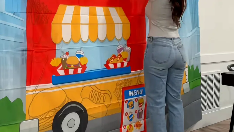 Woman in jeans hanging a food truck party backdrop with a printed menu on a white wall