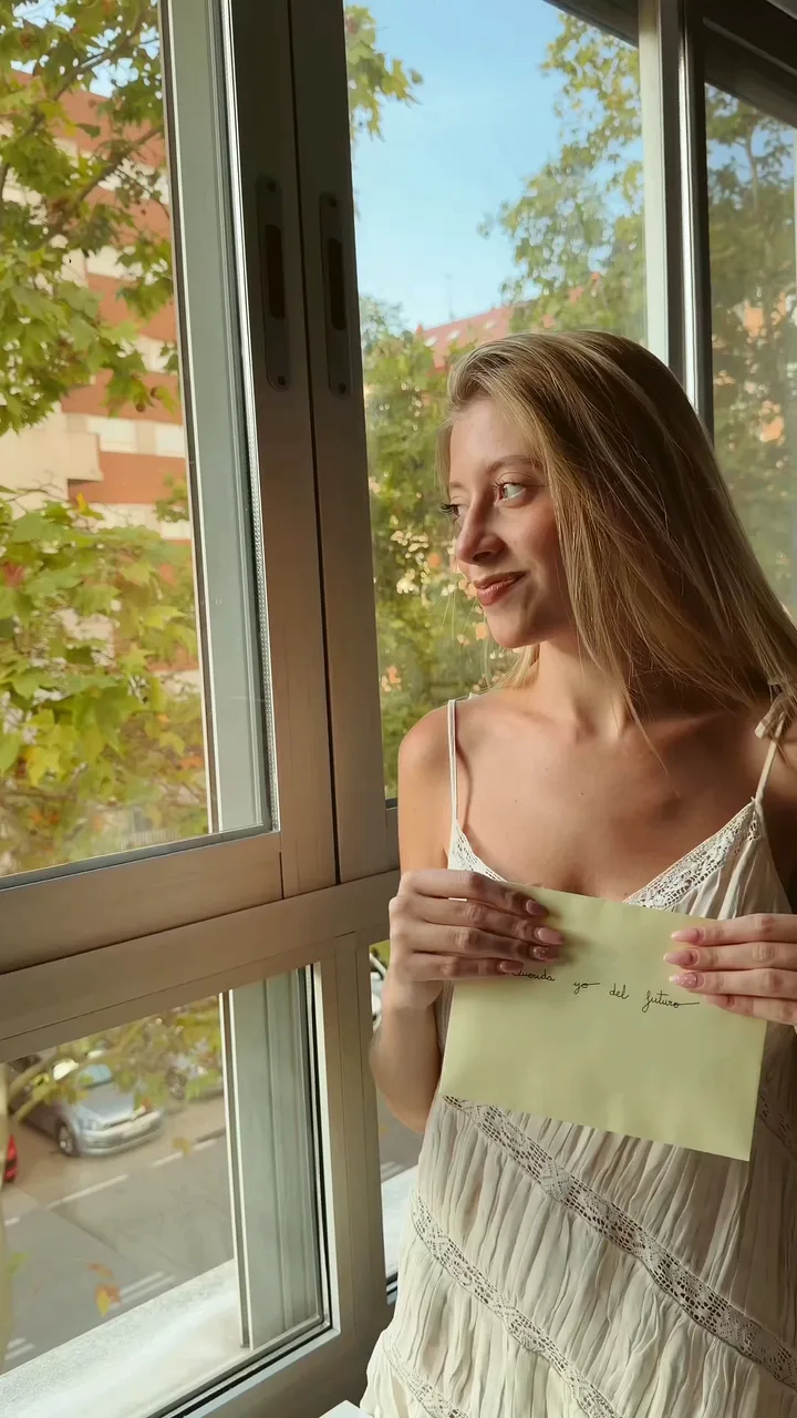 Woman in a white lace sundress holding a handwritten pale green envelope by an open window