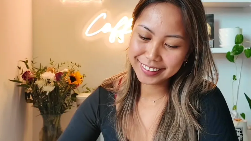 Smiling woman with long highlighted hair looking down in a home cafe corner with a neon coffee sign