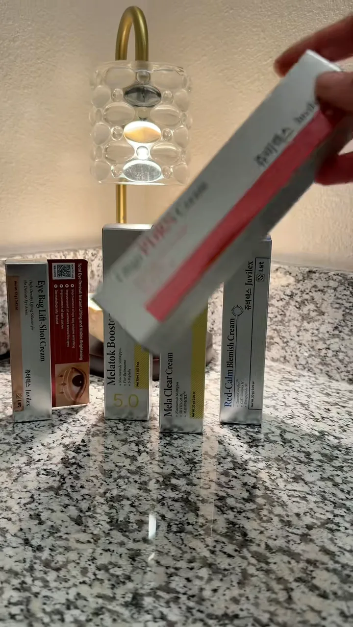 Hand lifting a Juvilex cream box from a row of skincare boxes lined up on a granite counter