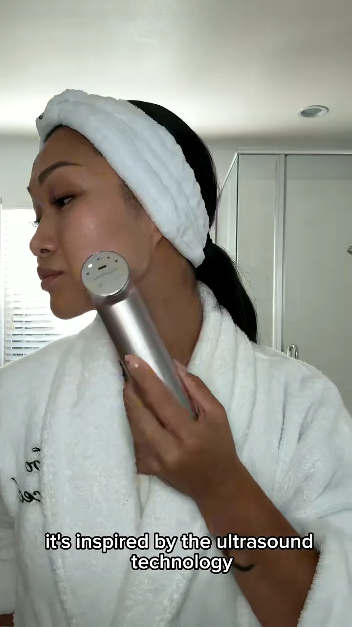 Creator in a robe and headband using a skincare device on her jawline