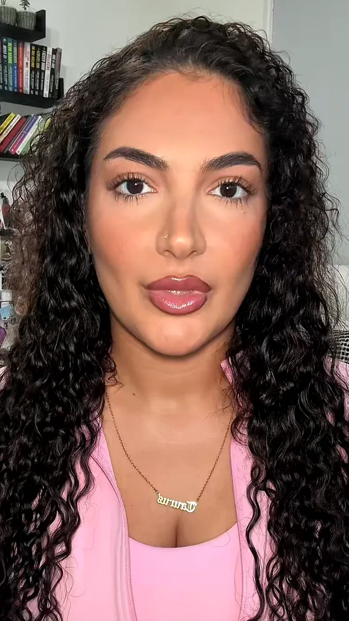 Woman with long dark curls and a gold name necklace talking straight to her phone camera